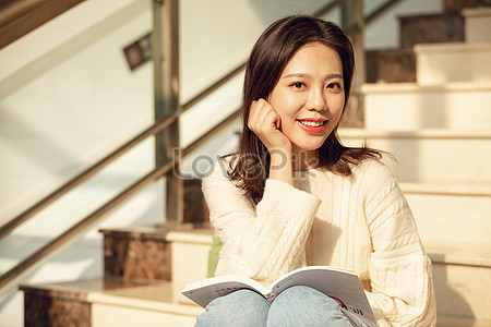 Image of A young woman sitting on a staircase reads a book