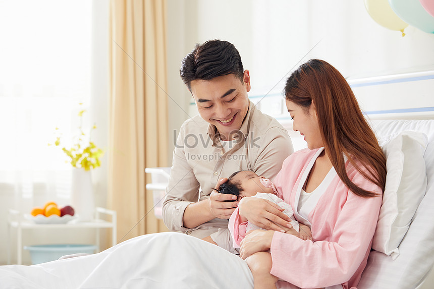 Young Father And Mother Taking Care Of Infant Baby In Hospital Bed