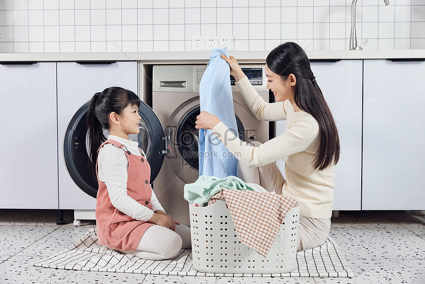 Mother And Daughter Put The Laundry In The Washing Machine To Wash