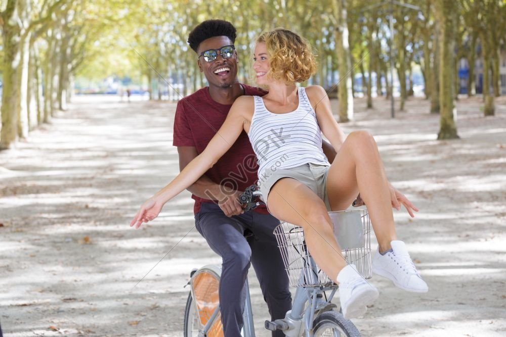 Joyful Couple Riding One Bike In A Public Park A Photo Picture And