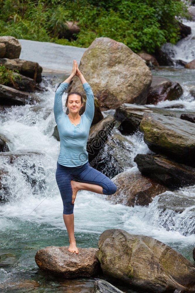 Woman in Hatha yoga balance yoga asana Vrikshasana tree pose at waterfall  outdoors - SuperStock