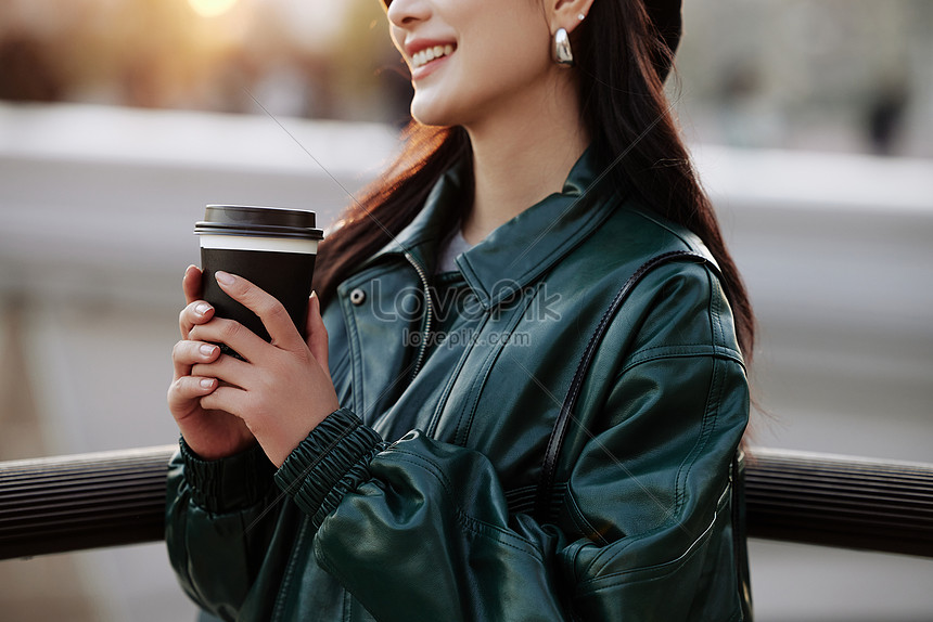 コーヒーを手に持って夕方に歩くファッショナブルな女性のクローズ