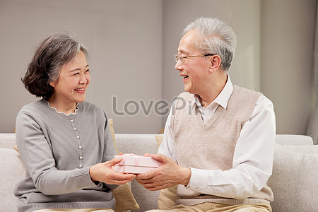 Elderly, couple and happy with gift, surprise and kiss on face together in  home. Man, woman and retirement show love, romance and happiness giving  present for anniversary, birthday or mothers day Stock